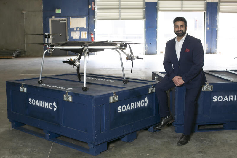 Amir Emadi in a suit beside the Gabriel autonomous cargo aircraft on Soaring flight cases.